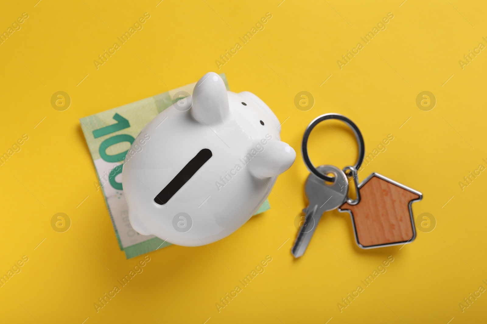 Photo of Ceramic piggy bank, euro banknote and key on yellow background, flat lay. Financial savings