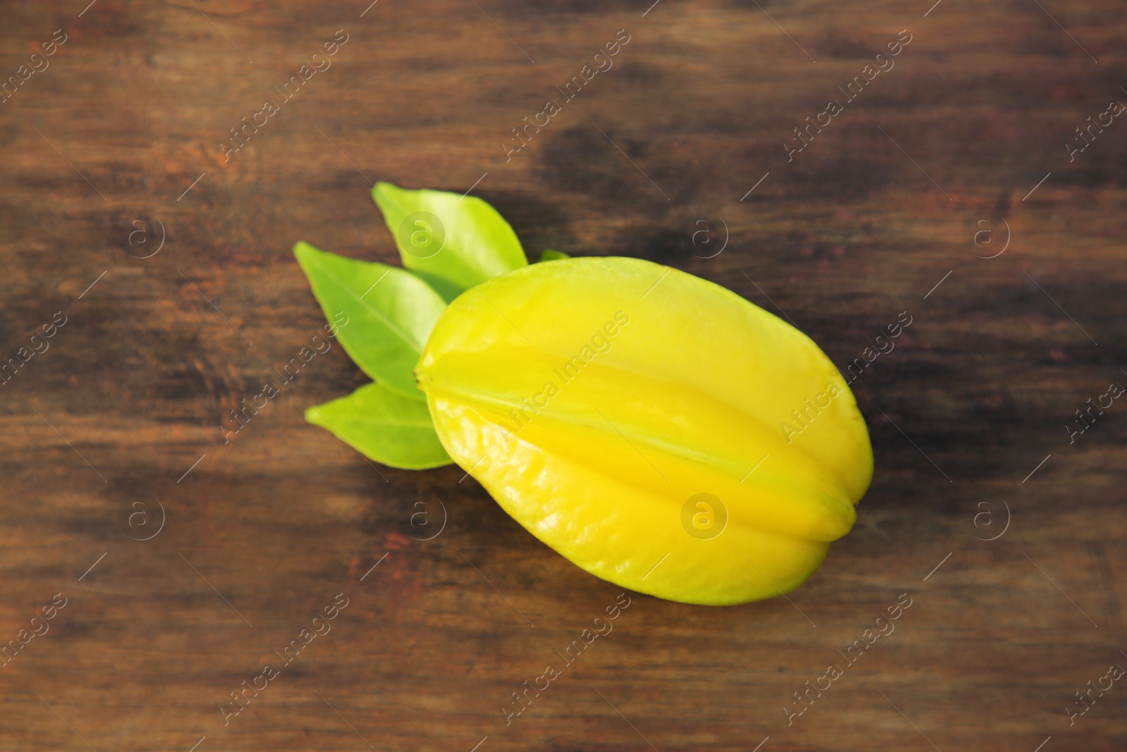 Photo of Delicious ripe carambola with leaves on wooden table, top view