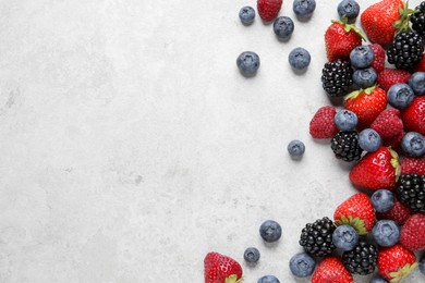 Many different fresh ripe berries on white textured table, flat lay. Space for text