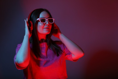 Stylish woman with headphones wearing sunglasses on color background, space for text