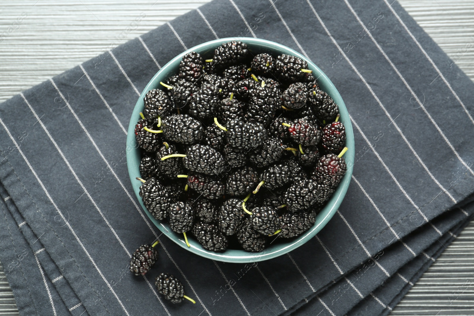 Photo of Bowl with delicious ripe black mulberries on dark wooden table, flat lay