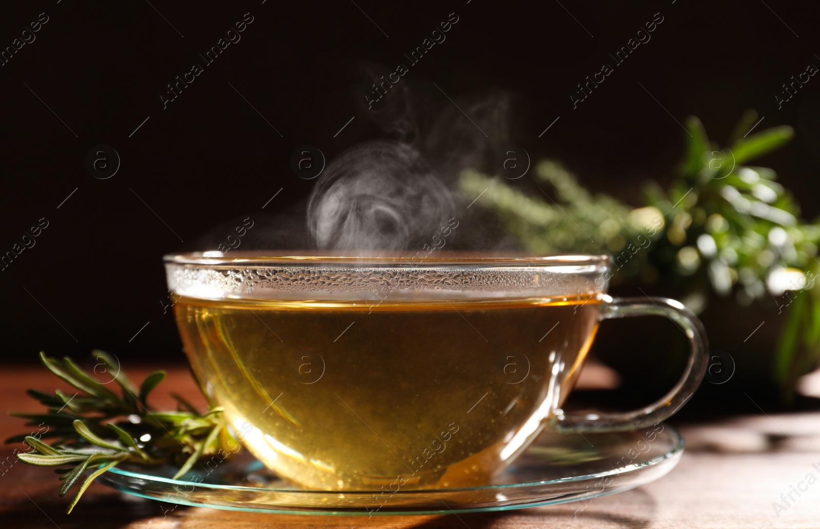 Photo of Cup of aromatic herbal tea and fresh rosemary on wooden table, closeup