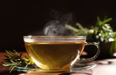 Cup of aromatic herbal tea and fresh rosemary on wooden table, closeup