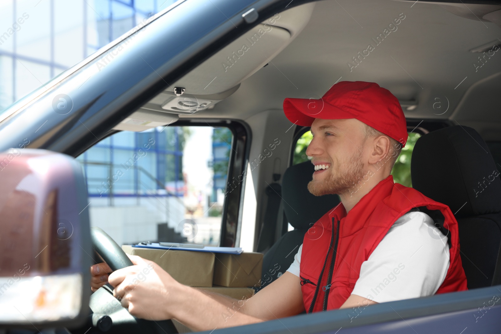 Photo of Young courier with parcels in delivery car