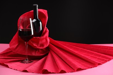 Photo of Stylish presentation of delicious red wine in bottle and glass on pink table against black background. Space for text