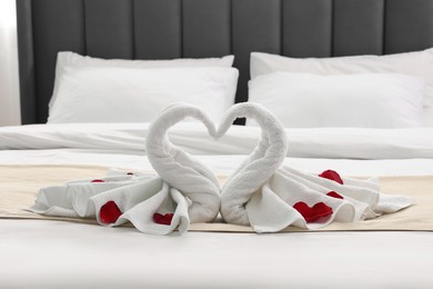 Honeymoon. Swans made of towels and rose petals on bed in room