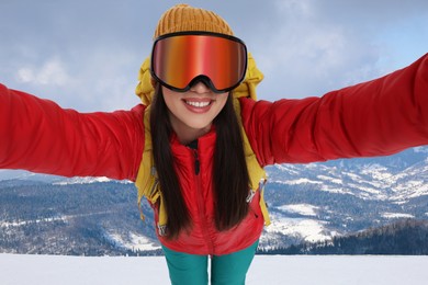 Image of Smiling woman in ski goggles taking selfie in snowy mountains