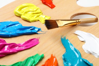 Photo of Palette with paints and brush on white background, closeup. Artist equipment