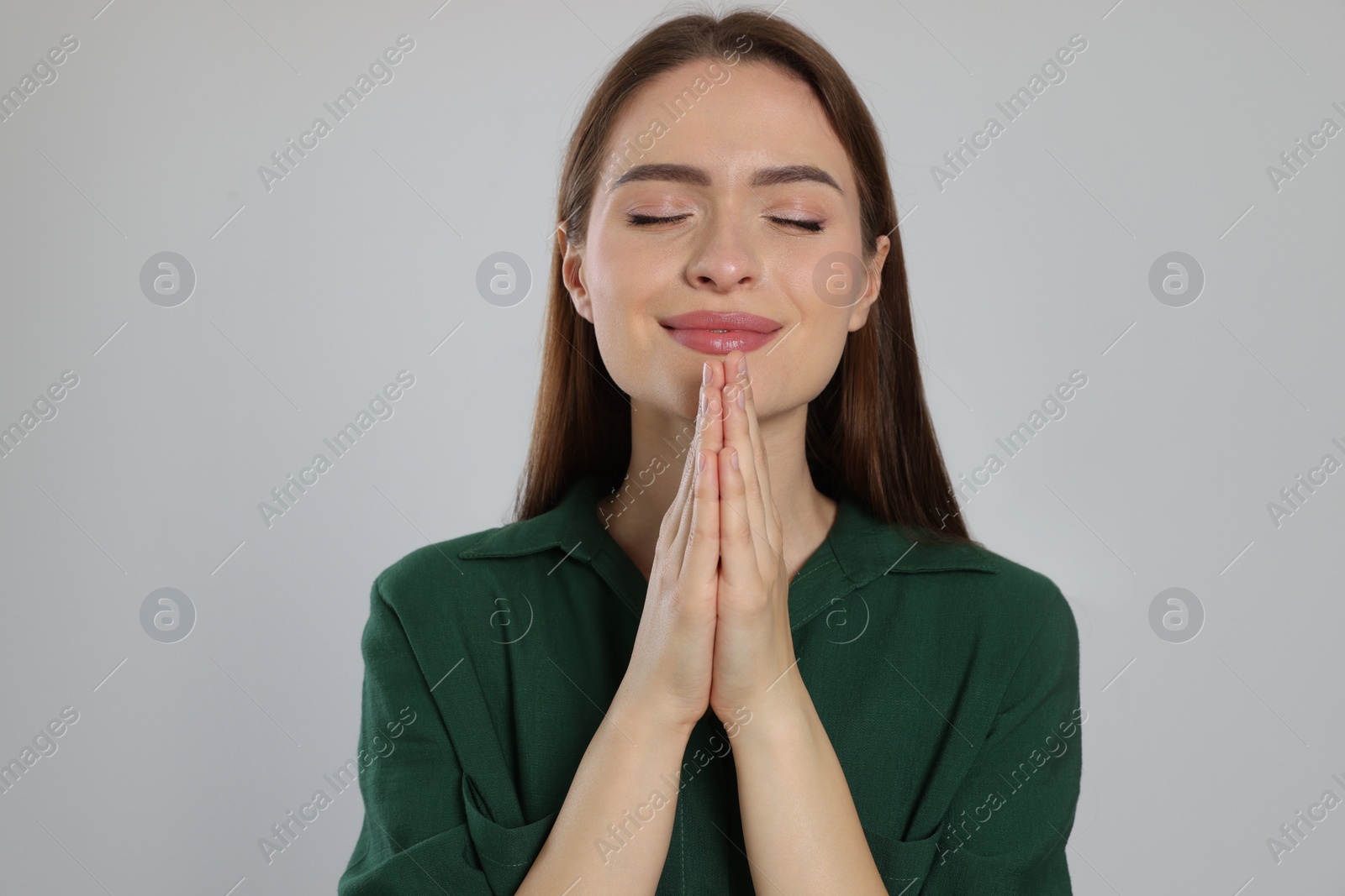 Photo of Woman with clasped hands praying on light grey background