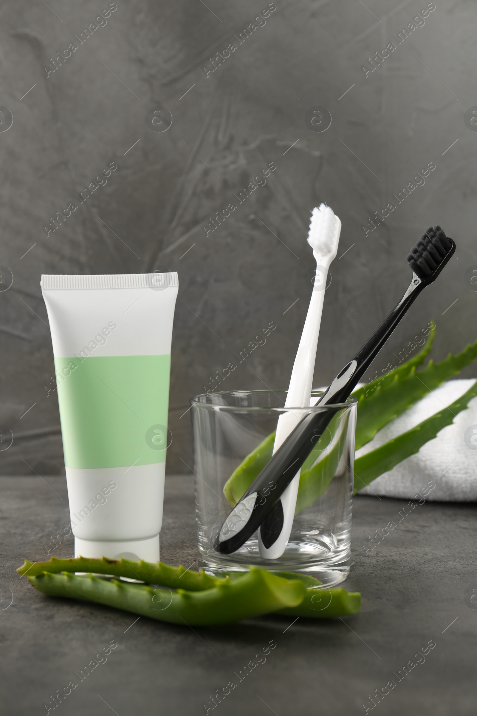 Photo of Aloe vera toothpaste in blank tube, brushes and green leaves on grey table. Space for text