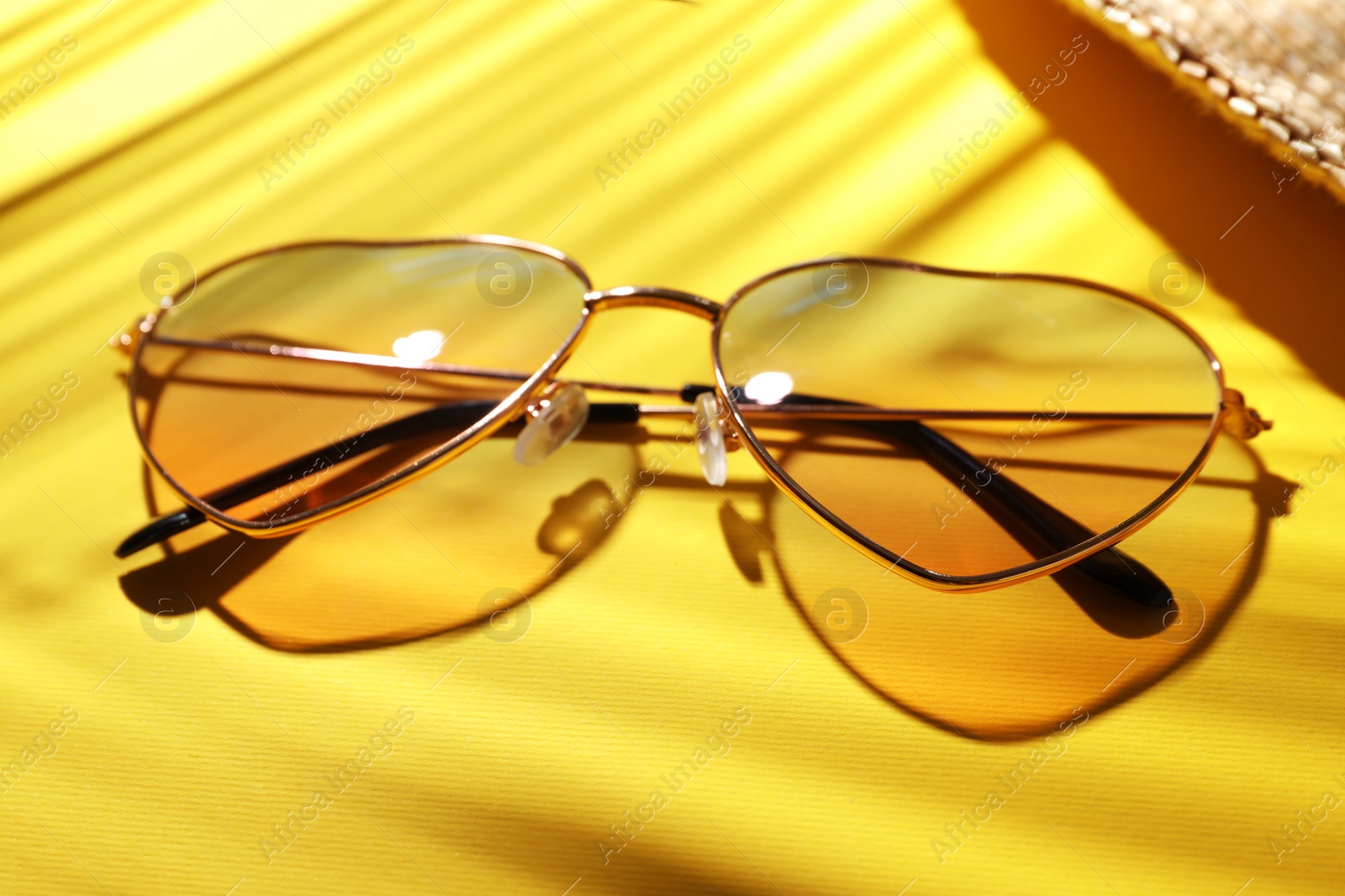 Photo of Stylish elegant heart shaped sunglasses on yellow background, closeup