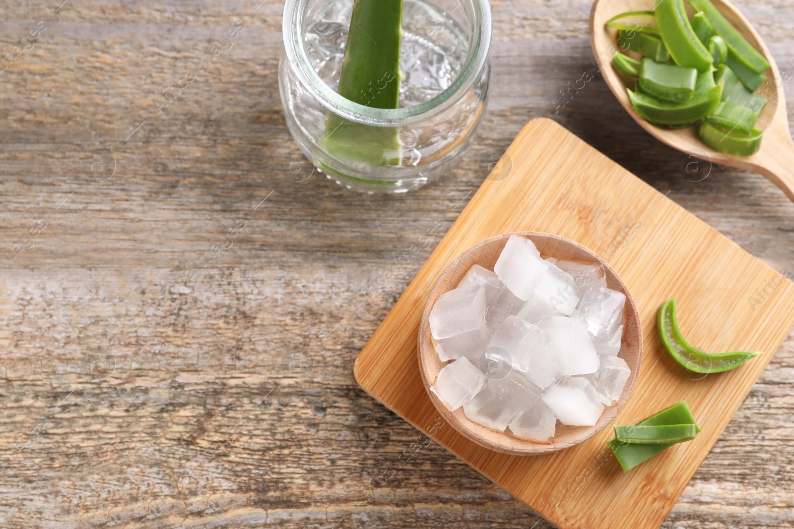 Photo of Aloe vera gel and slices of plant on wooden table, flat lay. Space for text