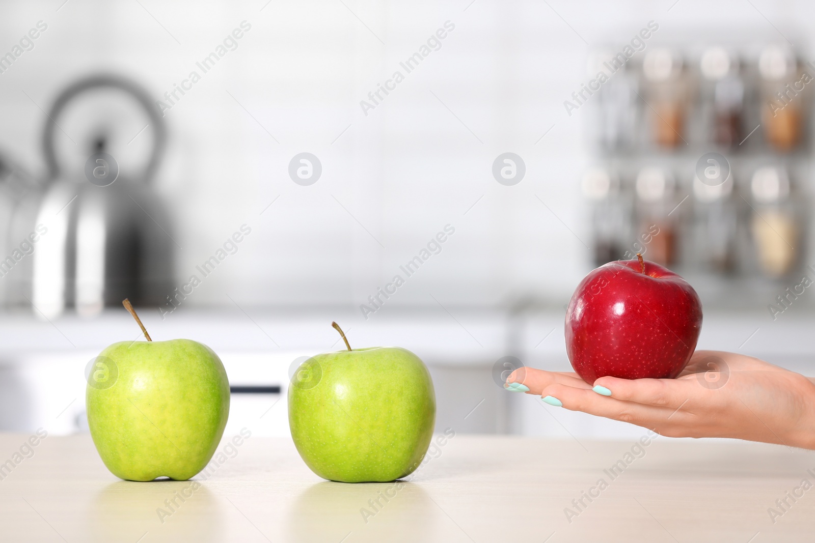 Photo of Woman holding ripe apple above kitchen counter, closeup. Space for text