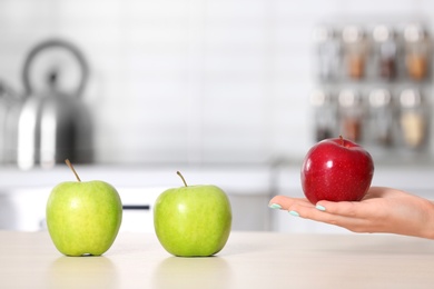 Woman holding ripe apple above kitchen counter, closeup. Space for text