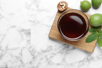 Photo of Delicious liqueur and fresh walnuts on white marble table, flat lay. Space for text