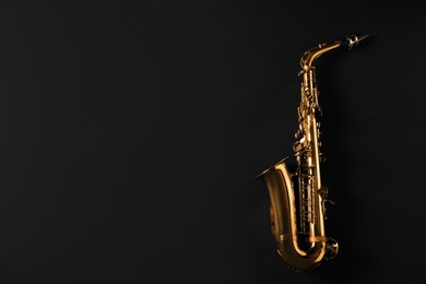 Photo of Beautiful saxophone on black background, top view. Space for text