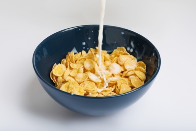 Photo of Milk pouring into bowl with crispy cornflakes on white background