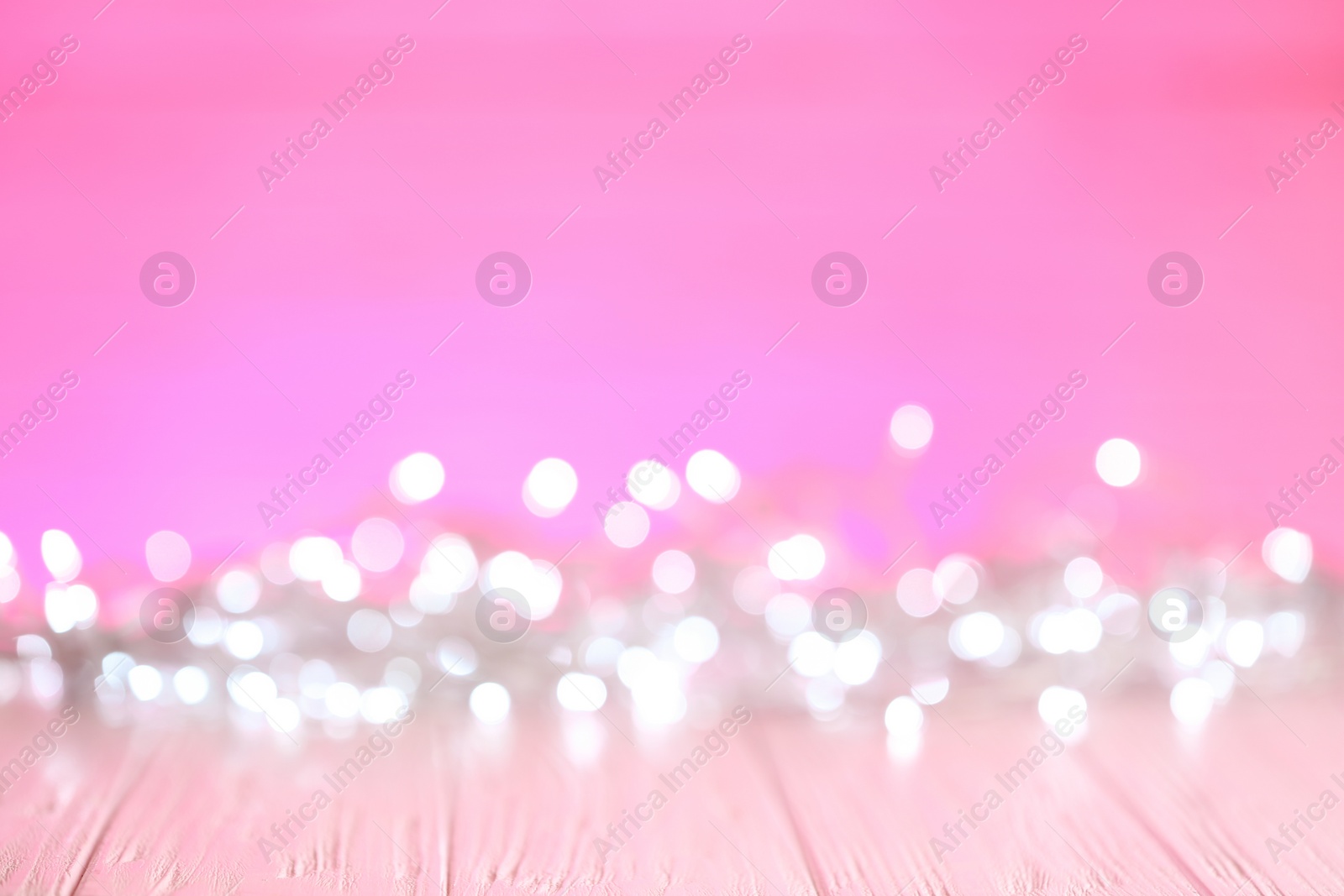 Photo of White Christmas lights on pink wooden table, blurred view