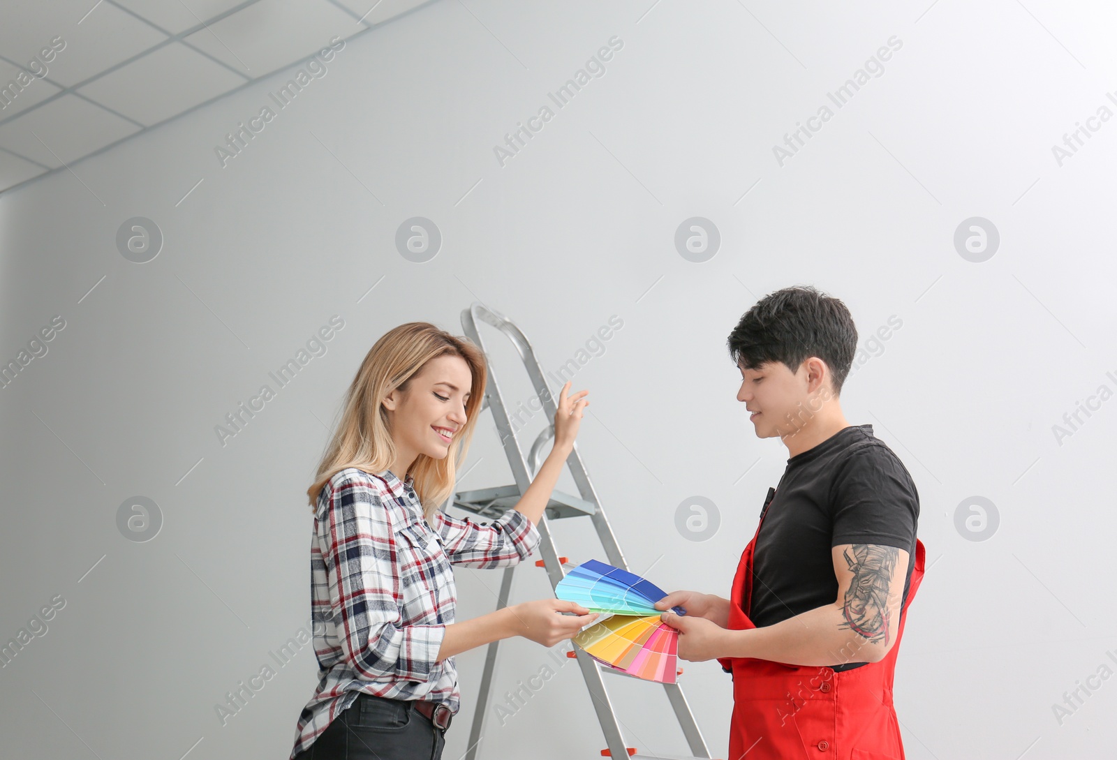 Photo of Male decorator and young woman choosing color for walls in empty room