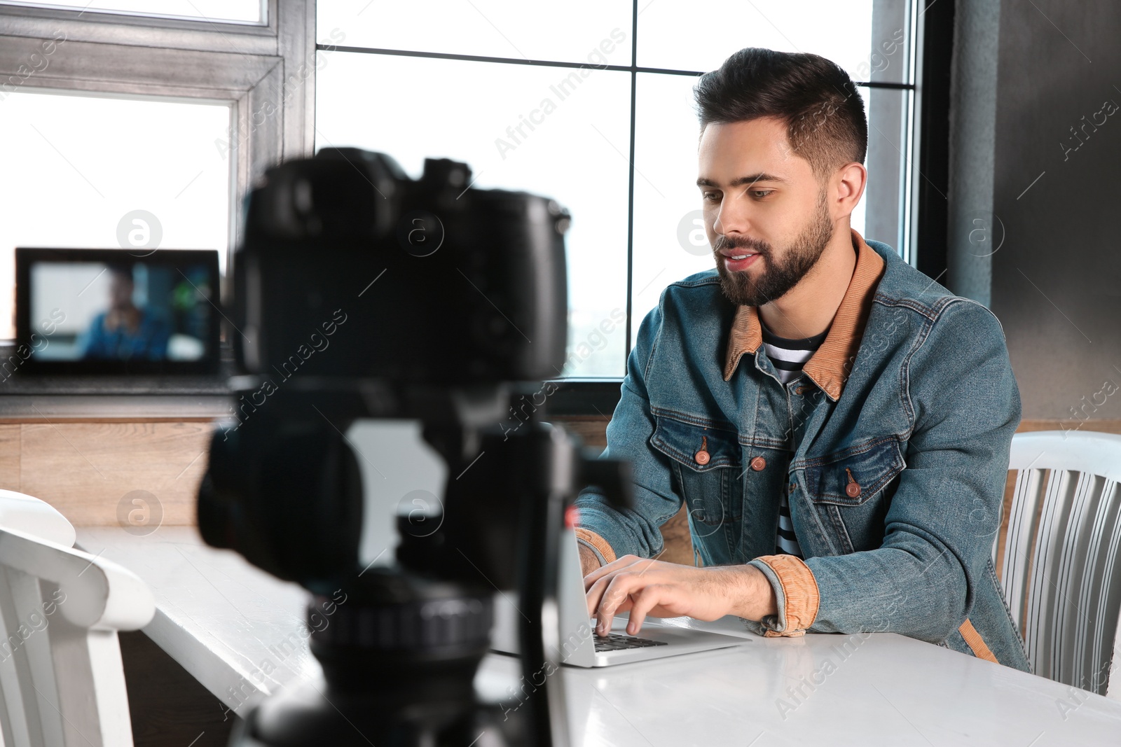 Photo of Young blogger with laptop recording video on camera at cafe