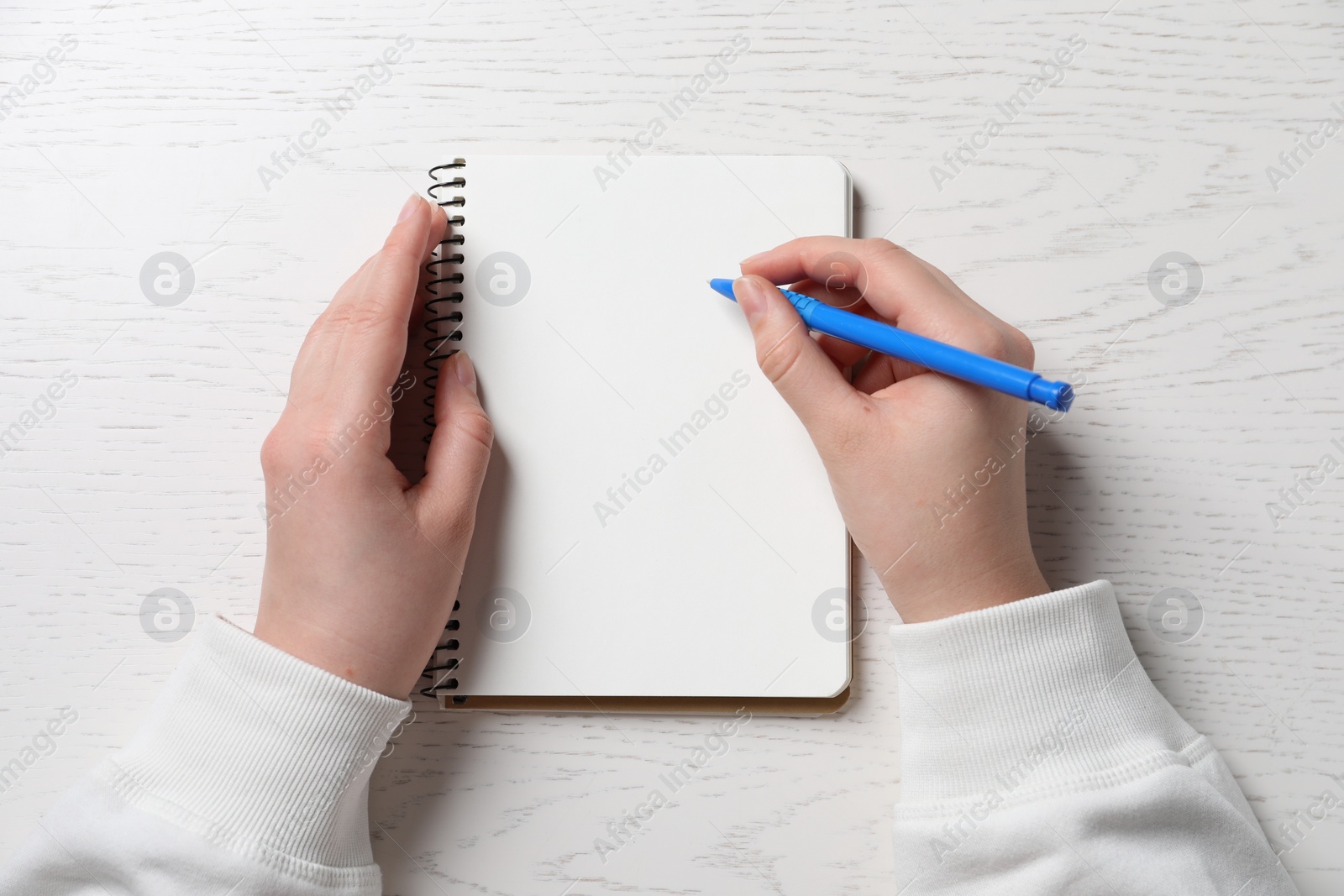 Photo of Woman writing in notebook with pen at white wooden table, top view