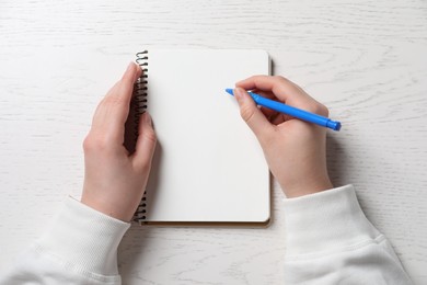 Woman writing in notebook with pen at white wooden table, top view