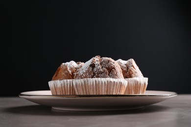 Photo of Tasty muffins with sugar powder on grey textured table, closeup