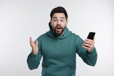 Shocked young man using smartphone on white background