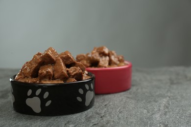 Wet pet food in feeding bowls on grey table. Space for text