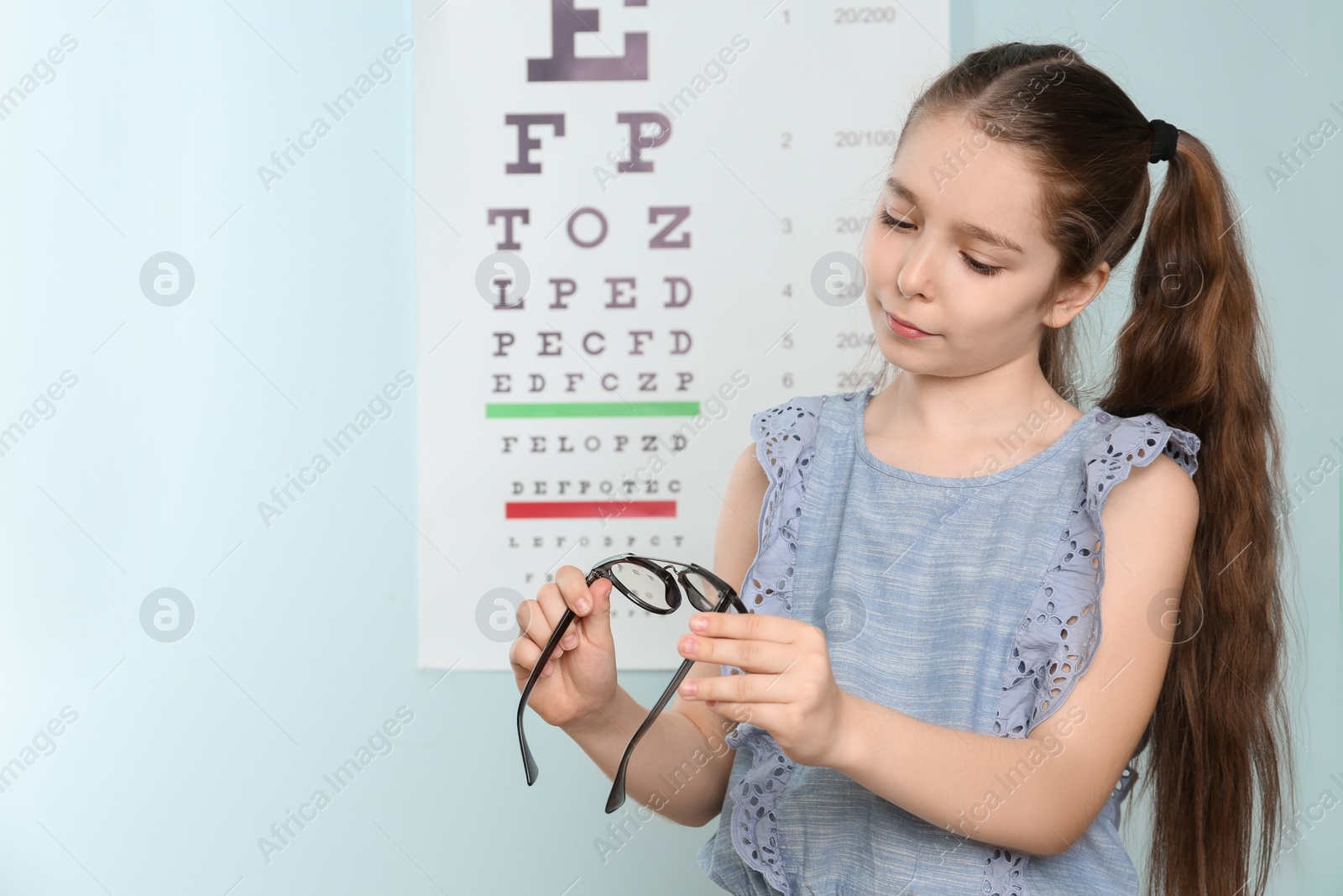 Photo of Cute little girl with eyeglasses in ophthalmologist office