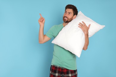Photo of Smiling handsome man with soft pillow pointing on light blue background, space for text