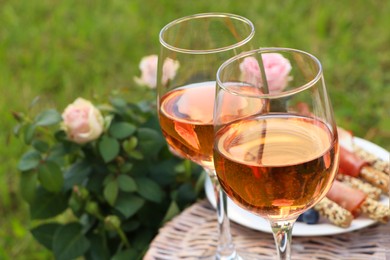 Glasses of delicious rose wine and food on picnic basket outdoors, closeup