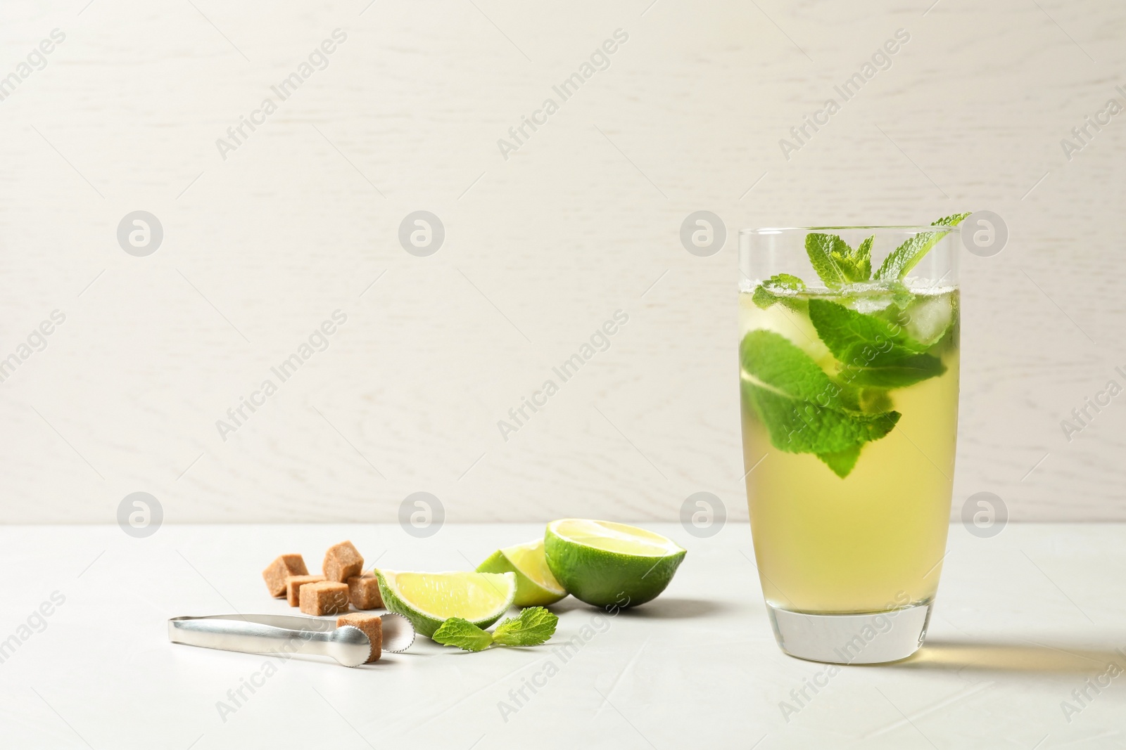 Photo of Glass with aromatic mint tea, fresh leaves, lime and sugar cubes on table