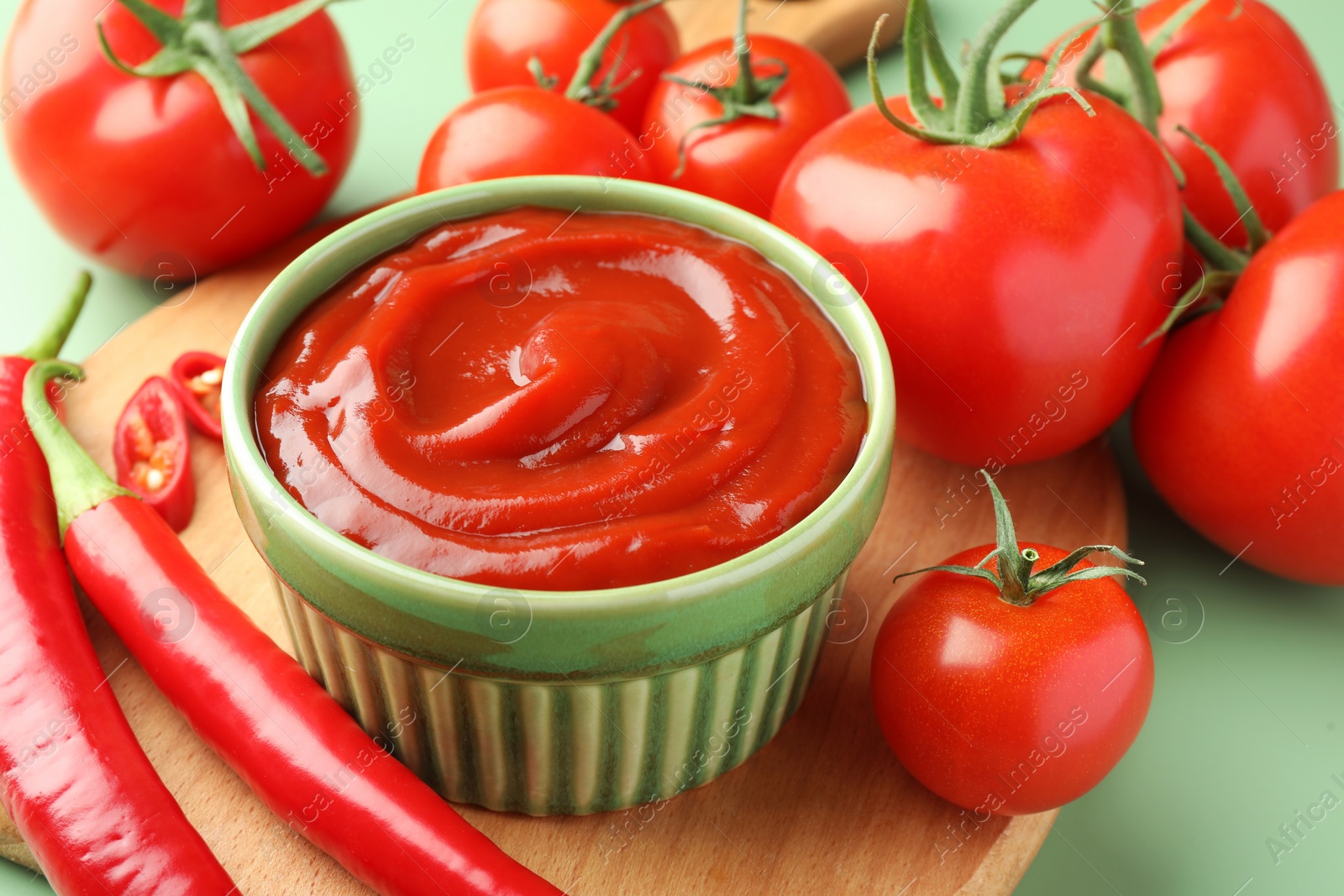 Photo of Bowl of tasty ketchup and ingredients on green table, closeup