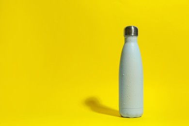 Photo of Stylish light blue thermo bottle with water drops on yellow background, space for text