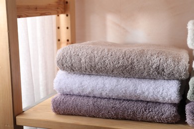 Photo of Stacked soft towels on wooden shelf indoors