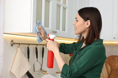 Photo of Woman cleaning furniture with rag and spray bottle in kitchen