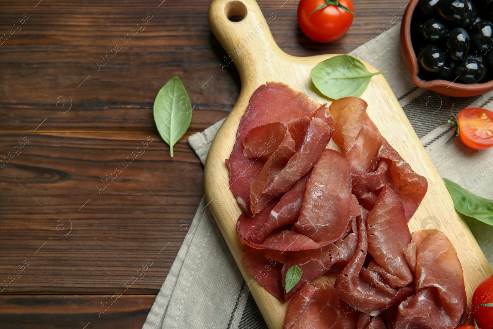 Photo of Board with delicious bresaola and other snacks served on wooden table, flat lay. Space for text