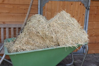 Wheelbarrow with hay near wooden stable outdoors, closeup