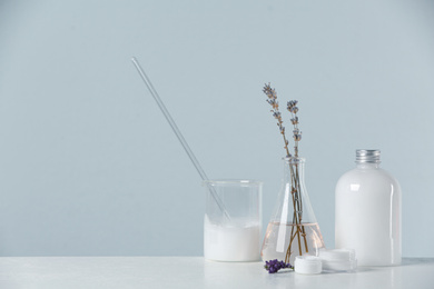 Herbal cosmetic products, laboratory glassware and ingredients on white table, space for text