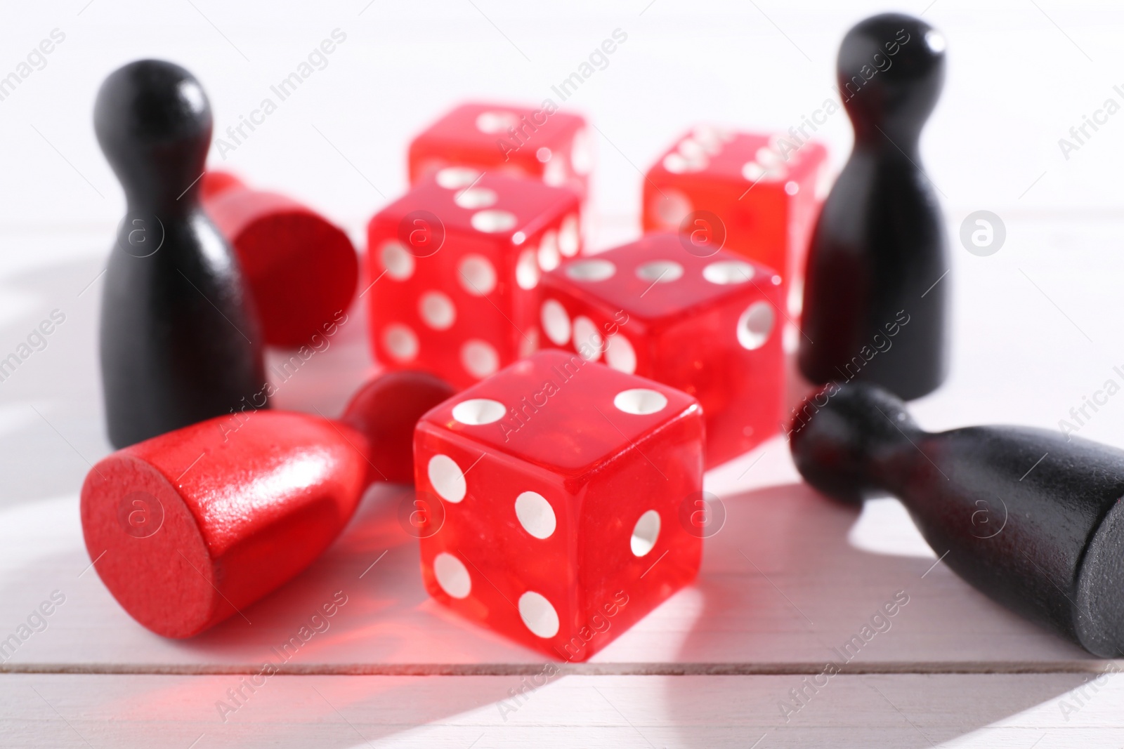 Photo of Red game dices and color pieces on white wooden table, closeup