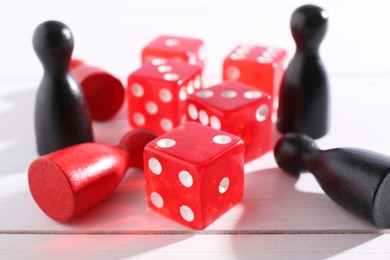 Red game dices and color pieces on white wooden table, closeup