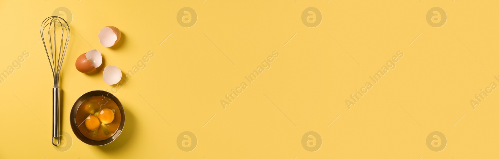 Image of Metal whisk, raw eggs and shells on yellow background, flat lay. Banner design with space for text