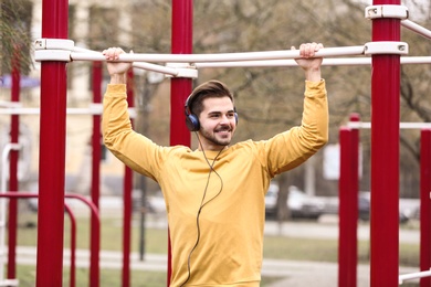 Photo of Young man with headphones listening to music and exercising on sports ground