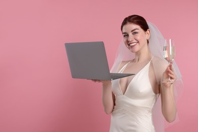 Happy bride with laptop and glass of sparkling wine on pink background