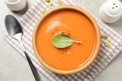 Photo of Tasty creamy pumpkin soup with basil in bowl on grey table, flat lay