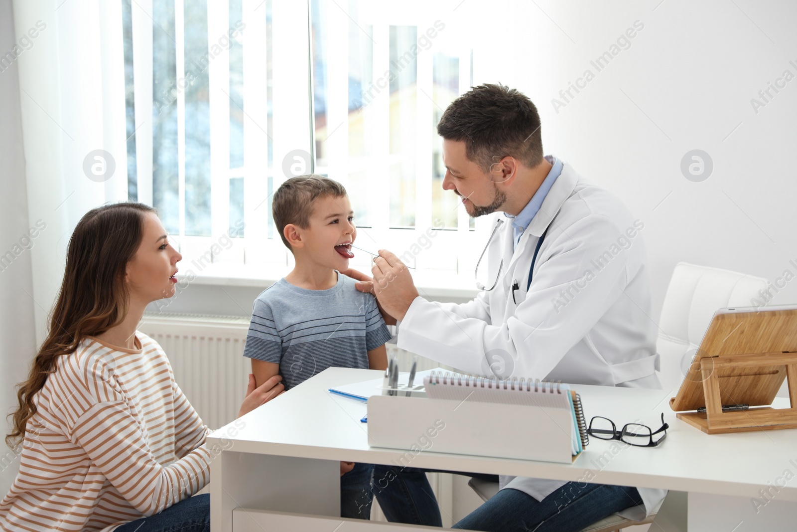 Photo of Mother and son visiting pediatrician. Doctor examining little patient's throat in hospital