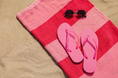 Photo of Beach towel with slippers and sunglasses on sand, top view. Space for text