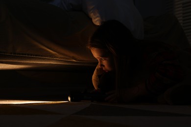 Little girl with flashlight looking for monster under bed at night