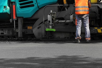 Photo of Worker working with asphalt finisher on city street, closeup. Road repair service